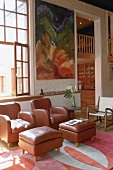 A pair of leather armchairs and footstools in a high living room with a view through a doorway