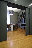 A designer apartment - a grey wall with a sliding door, a continuous parquet floor and a view into a living room