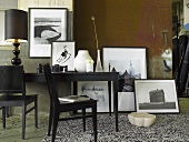 Schwarze Stühle vor Wandtisch mit schwarzer Tischlampe und gerahmten Fotografien