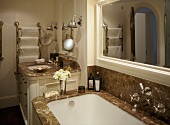A detail of a traditional bathroom, showing a fitted bath with marble surround, wash basin set in unit, mirror