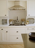 A detail of a modern, country kitchen with painted units, stainless steel gas hob, extractor fan