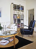 A modern, sitting room, bookcase, books, sofa, leather arm chair, rug, glass coffee table, candles, candlestick, plant,