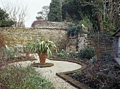 Walled garden with a pot plant central to a gravel path.
