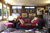 A sofa with lots cushions surrounded by framed pictures and next to a wall of vinyl records within a shed.