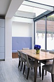 Vase of blue flowers on wooden table and chairs in contemporary dining room
