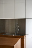 A sink with a tap against a stainless steel splash guard with white fitted cupboards above