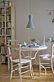 A coffee break on a white wooden table with wooden chairs and a 1950s-style pendant lamp hanging above