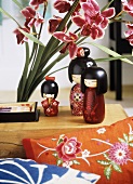 A detail of Japanese styled sitting room, wooden painted dolls, embroidered cushion, pink flowers,