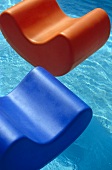Orange and blue plastic floating chairs in outdoor swimming pool