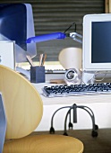 A detail of a modern home office showing a desk, computer screen, keyboard, wooden chair