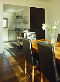 Wooden dining table with black leather dining chairs with view to kitchen beyond