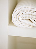 Bedroom detail of white cotton bedcover on shelf.