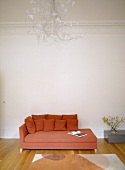 A detail of a modern, sitting room with a red upholstered sofa, chaise longue, wood floor, side table, chandelier light,