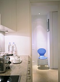 A detail of a modern kitchen in neutral colours, granite work top, toaster, blue retro chair seen through open doorway,