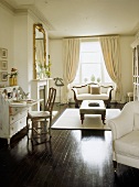 A traditional, white sitting room, polished wood floor, painted bureau, gilt chair, upholstered armchair, rug, open curtains,