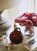 A display of items on a table including a vase of pink roses, a stone lamp, a silver box and a glass bottle