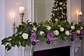 A flower arrangement and burning candles in silver candlesticks on a white mantelpiece