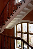 Staircase with wooden banister on the stairs and red-brown wall