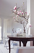 A magnolia sprig in a glass vase on an antique table in a white room