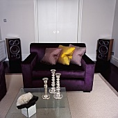 Silberne Kerzenständer auf Glastisch vor lila Sofa mit Seidenkissen in moderne Wohnzimmer