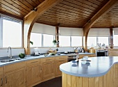 Holzdecke im kreisförmigen Raum mit offener Küche aus hellem Holz und geschwungenem Küchenblock