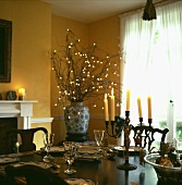 Kerzenleuchter auf gedecktem Tisch und Lichtdeko in Vase im gelben Esszimmer