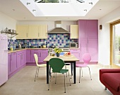 Verschiedenfarbige Stühle im Bauhausstil und Holztisch unter Oberlicht in moderner Küche mit rosa Holzfronten