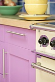 Herdgriffe eines Küchenofens neben Küchenschrank mit rosa Holzfront