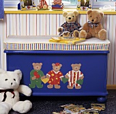 Blaue Holztruhe mit aufgemalten Teddybären und einem gestreiften Sitzkissen, darauf sitzen Teddybären