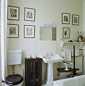 Traditionelles, weisses Badezimmer mit kleinem antiken Holzschrank, einem weissen Stand-Waschbecken und schwarz-weiss Drucken an der Wand