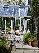 Terrasse mit weissen, metallenen Gartenmöbeln vor einem gläsernen Wintergarten