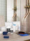 A tiled bathroom with taps and bathing utensils in front of a mirror