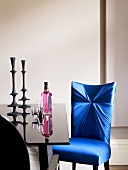 A chair with a blue cover with a Pink Gin and candle sticks on a black table