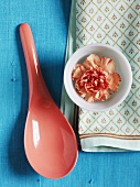 A carnation in a bowl with a spoon and a cloth on a blue surface