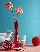 A pomegranate, pomegrante juice and carnations in a vase against a blue background