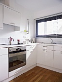 A corner of a kitchen with white cupboards and closed blinds