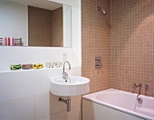 A modern bathroom with light brown wall tiles around a bathtub and a designer wash basin with a mirror