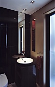 A corner of bathroom with a wash basin and a designer mirror