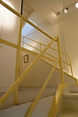Weisses Treppenhaus mit gelber Metall-Geländer und Deckenstrahler