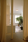 Cremefarbene Vorhänge vor dem Badezimmer mit weißem Fliesenboden und grossen Zimmerpflanzen