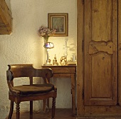 Holzstuhl und Tisch mit brennender Lampe neben einer alten geschnitzten Holztür