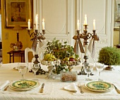 Festlich gedeckter Tisch mit Kerzen in hohen Kandelabern und Obst-Dekoration auf weißem Tischtuch