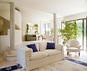 Blaue Zierkissen auf Sofa und blaue Teppichbordüre als Farbtupfer im Weiß des modernen, offenen Wohnzimmers