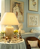 Brennende Lampe mit Vasenfuss auf kleinem Tisch mit dekorierten Taschenuhren vor Frauenportraits und Frauenbüste