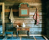 Kleiner bemalter Hängeschrank, Tisch und blauer Stuhl vor horizontal verkleideter Holzwand in Holzhaus