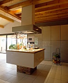 Auf Backsteinsockel schwebende Kochinsel unter Dunstabzugshaube mit integrierten Strahlern in minimalistischer, offener Küche