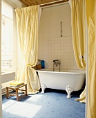 Lange, gelbe Vorhänge vor freistehender Badewanne mit Klauenfüssen auf blauem Teppich in traditionellem Bad