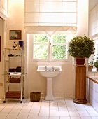Weisses, französisches Altbau-Bad mit Faltrollos vor Sprossenfenstern, Metallregal und Pflanze auf Holzsäule