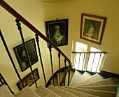 Viktorianische Portraits hinter zierlichem, antikem Geländer in mit Teppich belegtem, gewendeltem Treppenaufgang