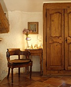 Antiker, hölzerner Sessel und Tisch mit brennender Lampe neben alten geschnitzten Türen eines Einbauschranks